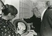 Interiör. Kung Gustav VI Adolf på besök i Gustavsbergs Fabriker. Formgivaren Britt-Louise Sundell förevisar kungligt porslin, sannolikt på Porslinsmuseet, i Gula huset,, Gamla kontorets kyrksal.
Personer: Kung Gustav VI Adolf och Britt-Louise Sundell