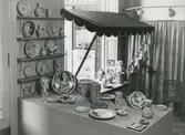 Interiörbild. Utställning med föremål från Gustavsbergs fabriker. Fat och vaser. Fajanser målade i rödlera, polykrom dekor. Konstnärer: Wilhelm Kåge och Stig Lindberg. 1942. Plats okänd.