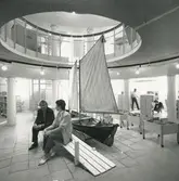 Interiörbild. Runda huset  inför invigningen som kuturhus och bibliotek. Singösnipan Elvira byggd i mindre format anpassad till bibliotekets barnavdelning. Tina Norderheim -Lindemalm och Åke Axelsson, inredningsarkitekt.
Personer: Tina Norderheim-Lindemalm och Åke Axelsson, inredningsarkitekt.