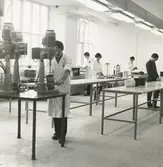 Interiör. Materiallaboratoriet. Utförande av materaltester.
Personer: okända