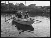 Fyra kvinnor i en roddbåt. Ankrade fiskebåtar i bakgrunden. Troligen Fiskebäckskil, Bohuslän.