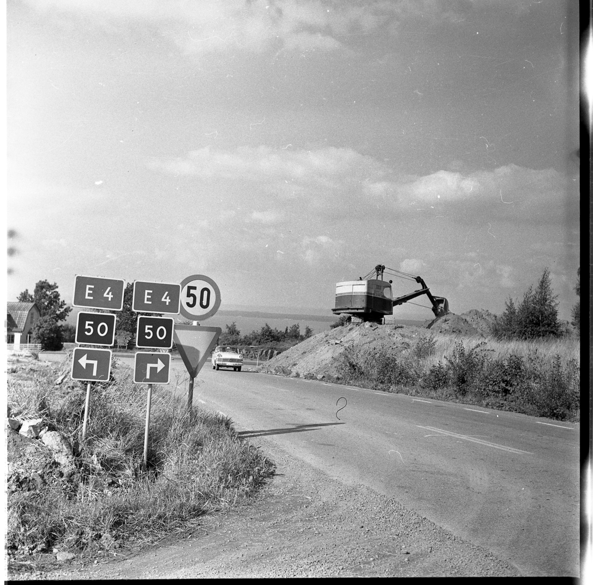 Percy Heldebrandt, Väghänvisningar mot E4:an och väg 50 vid Galgen. En Opel kommer åkande mot fotografen och på en höjd till höger arbetar en grävskopa, i samband med motorvägsbygget vid Gränna/Röttle, etapp II.