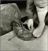 Personvagnsreparatör Einar Larsson, vid Trafikaktiebolaget Grängesberg–Oxelösunds Järnvägars järnvägsverkstad i Eskilstuna, demonstrerar hur skyddsskon räddade hans tår i samband med en arbetsplatsolycka då en 150 kilos buffert föll ner på hans fot.