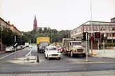 Vy mot Fässbergs kyrka, okänt årtal. Göteborgsvägen ses främst i bild och bilar köar på Tempelgatan (vänstertrafik), för att köra över vägen. Till höger: Mölndals Taxistation och bakom denna skymtar Mölndals stadshus.