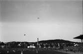 Fotbollsmatch på gamla Ryavallen i Borås, uppförd 1941. Ett par knippen med ballonger stiger till väders, en orkester spelar medan ena laget springer in på plan. Bakom stadion syns villabebyggelsen och en skorsten.