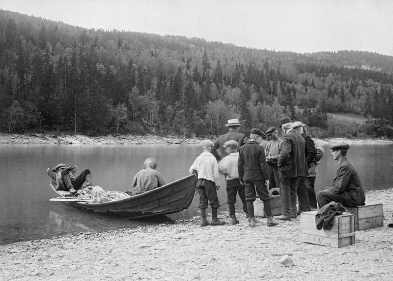 Notfiske etter lågåsild (Coregonus albula) i nedre del av Gudbrandsdalslågen, nærmere bestemt ved Tråset i Fåberg.  Fotografiet antas å være tatt mellom 1915 og 1920.  På elvebredden var det ni personer – guttunger og voksne menn – som hadde samlet seg rundt trekasser med nyfanget fisk.  Inne på elvebredden sto det trekasser som fangsten skulle samles i.  Til venstre i bildet ser vi ei åfløy, den karakteristiske flatbotnete båttypen som var tilpasset dette elvelandskapet med sine mange grunne partier med sand- og grusøyrer.  Da dette fotografiet ble tatt lå det ei not i midten av båten.  En mann satt framfor denne.  I «plitten» (akterenden) lå en unggutt og kvilte. Huitfeldt-Kaas beskrivelse av lågåsildgarn og fiskeprosedyrer knyttet til denne redskapstypen er gjengitt under fanen «Opplysninger».