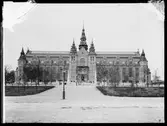 Nordiska museets huvudbyggnad strax före färdigställandet och invigningen 1907. Framför byggnaden står några förbipasserande människor och betraktar byggnadsarbetarna som står på ställningar framför entrén och tornen.