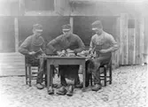 Larsson och Hallbergs Toffelverkstad (f.d. Andersson och Sjöbäck) på Torggatan 19, Varberg. År 1904. Från vänster; Birger Bengtsson, Axel Bartholdsson och Frithiof Hallberg. De sitter vid ett bord med tofflorna ute på en kullerstensbelagd gård.
