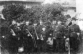 Gruppbild med 9 män samt 1 pojke, tillhörande gamla Skarpskyttekåren, stående med var sitt musikinstrument.
Musiken vid Alingsås.
