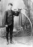 Reinhold Thorssin i knickers och mössa, fotograferad i en fotostudio, bredvid en höghjuling.
Bilden är felvänd.