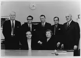 Gruppbild av de 7 ledamöter  i Konsums styrelse 1964 - fem stående män i kostym och två sittande kvinnor. 
Stående fr.v: Torsten Svärd, Åke Carlsson, Gustav Berg, Olof Borged, Sven Gustavsson. Sittande fr.v: Signe Petterson, Linnéa Fransson.
(se Kunsum Alingsås 50 år, 1915-1965. Alingsås musei bibliotek)
Originalbild mycket grått.