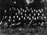 Gruppbild av ett 40-tal kvinnor och män tillhörande Frälsningsarméns hornmusikkår, sittande och stående, med sina musikinstrument. Kvinnorna i hätta/bahytt och männen i uniformsmössa.