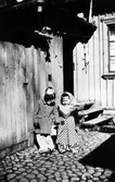 Två stycken påskkärringar står vid en träbeklädd vägg. Till höger: Nils-Arne Sandberg.

Kvarteret Storken, Nygatan 11.