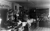 Inifrån K.P. Wessmans speceriaffär. En överblick av hyllor med livsmedel av alla dess slag. Bakom disken står Hanna (Johanna) Wessman.