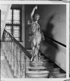 Skulptur i trapphuset, troligen i fastigheten i hörnet av Drottninggatan-Tegnérgatan, med entré från Drottninggatan 87. I fonden syns målade glasfönster i trappan. Fastigheten revs för nya Postbankshuset. Foto 1959.