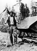 En rallare står vid sidan av en räls med en tippbar järnvägsvagn vid sin sida.
Troligen ej Alingsås.