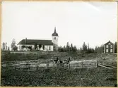 Hed sn, Hed kyrka.
Kyrka och bostad i bakgrunden. I förgrunden åker och en man med hästkärra.