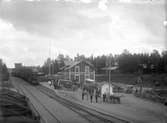 Stationen med resande. Bilar och bussar och ångtåg på stationen.