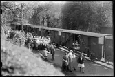 Tjustdräktklädda kvinnor vid Falerum station 22 juni 1933 på väg till Västerviksutsällningen. På spåret syns vagnar från Norra Östergötlands Järnväg, NÖJ.