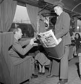 Tågbud säljer tidningar i SJ vagn typ Bo5b. Arrangerad bild. 
En av tidskrifterna i tågbudets väska är Life från 5 september 1949.