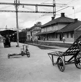 Stationshus i trä. I bakgrunden järnvägsrestaurang, hotell och nattväntsal . På plattformen står en trampdressin.