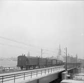 Statens Järnvägar SJ 1856-1956. 100-årsjubileum. Tåg med gamla lok och vagnar på Södra Järnvägsbron på sträckan mellan  Mälarstrand och Riddarholmen.