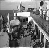 Tågfärjan Drottning Victoria,  däcksmotiv. Färjeläget i Sassnitz. Hjälpkryssaren Drottning Victoria var en svensk tågfärja tillhörande Statens Järnvägar. Drottning Victoria trafikerade normalt linjen Trelleborg – Sassnitz. Den medverkade som hjälpkryssare i svenska marinen under andra världskriget.   På bilden syns passagerarna som njuter i fulla drag på färjedäcket.