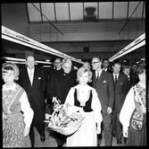 Invigning av Årsta partihandel. Kung Gustav VI Adolf, 3:a från höger bakom kvinnorna i folkdräkt. Kvinnor i folkdräkt med blomsterkorgar