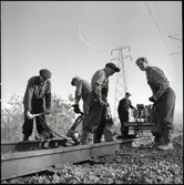 Banarbetare justerar ballasten under spåren med  vibratorspett.