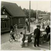 Bäruppköpare framför stationshuset. Häst med vagn, bilar och cyklar i bakgrunden.