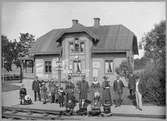 Kvinnor, män och barn uppställda framför stationshuset för fotografering.