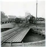 Påeldat lok framför lokstall. Personal utför service på loket.