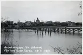 Arbetsbrygga för pålningsarbete för byggande av bro över Ätran. Falkenbergs gamla kyrka, S:t Laurentii, syns i bakgrunden.