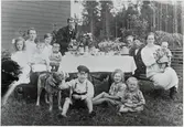 Kafferep i trädgården. Från vänster: Siri Andersson, Tekla Andersson med  Ingeborg i knät, Elna Sundquist med sonen Gösta i knät och Gustaf Sundquist, banvakt i Born. Sittande på marken: Folke, Anna-Lisa och Viola Johansson. På soffan till höger: David Johansson (Udd-Johans styvson), Arvid Johansson, banvakt i Lottbo, och Emma Johansson med Margit i knät.
