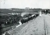 Gruslastat tåg som spårat ur på väg till Edsbyn. Järnvägen var 1900 nybyggd. Vid olyckan fick en man sin ena arm avsliten. I bakgrunden ses 
