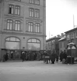 Hindersmässan i Örebro den 26 januari 1937. Folk är samlade invid Stora Hotellet strax intill korsningen mellan Engelbrektsgatan och Drottninggatan. I bottenvåningen på hotellbyggnaden ligger en fotoaffär. En bit bort på Drottninggatan kan man skymta en affärsskylt med namnet Oscaria. Detta är med största sannolikhet en skoaffär, eftersom Oscaria var namnet på en av Örebros största skofabriker. Längst till höger syns en gammaldags telefonhytt.