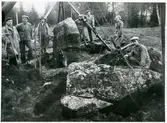 Badelunda sn, Anundshögsområdet, Långby.
Sten i skeppssättningen under resning. Kedjor runt stenen. Arbetere och besökare. Längst till vänster Sven Drakenberg. 1932.