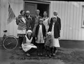 Emelie i Kalvhult står tillsammans med sju unga flickor och en liten pojke samlade på trappan till en byggnad med pardörrar. Kvinnorna är arbetsklädda med hucklen, förkläden och koftor. Flickan längst till vänster håller upp en handduk på en pinne likt en flagga.
