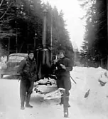 TVÅ MILITÄRER STÅR FRAMFÖR EN ÅNGKOKARE PÅ EN SKOGSVÄG.