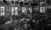 Verkstadsinteriör med axelledning i taket.
I verkstaden arbetar från vänster:
Evald Herngren, Axel Öst, John Fogelkvist, Arvid Pettersson, Johan Herngren och 
Sven Herngren.