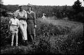 Paret Hellström med dotter vid en bergknalle i kohagen. Frun är klädd i en konstifik hatt och dräkt med klädda knappar och borderi på jackfickorna.
(Se även bildnr EA1041)
