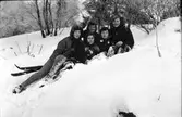 Fem skidåkerskor har tagit av skidorna och har lagt sig i en snöig skogsbacke.  Fr h: Birgitta Andersson, Inga-Britt Albinsson, Eivor Molin liggande framför Gullan Molin och längst till vänster en okänd flicka.
(Se även bildnr EA1055, EA1058)
