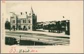 Vy på stationsområde med bebyggelse i bakgrunden.