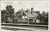 Spårsida av station och stationshus med del av perrong i bild.