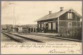 Stationsområde med resande och del av bangård i bild.