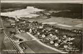 Flygvy på samhälle med järnvägsstation, jordbruk och kyrka vid Hillesjön.