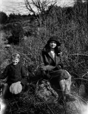 Emilia och Sten i Kålhagen sitter finklädda i solen på några stenar vid ett buskage.