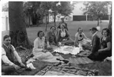 Picknick under Arbogautställningen 1935. Sju kvinnor och en man sitter på mattor utlagda i gräset. Avkoppling i Ahllöfsparken/Olof Ahllöfs park nära Arbogautställningen. De har kafferast i förberedelsearbetet inför utställningen.
Från vänster: Sven Drakenberg (intendent), Britta Orén, Olga Anderzon (från hemslöjdsföreningen), okänd, längst bak, i hatt,  Hanna Hartelius, Ulla Hermansson, Augusta Eriksson och Elin Höglund (konstnärinna)
Bildens baksida, se AKF-14500
Bilden är tagen av fotograf Blom i Västerås (förnamn saknas)