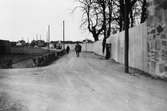 Här byggs Arbogautställningen. Planket leder fram till det som ska bli huvudentrén, i förlängningen av Dragmansgatan.
Grusväg. En bil och villor i bakgrunden.