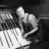 Arboga Tidning, interiör, personal. En man, med snickarbyxor och uppkavlade skjortärmar, arbetar vid en maskin.